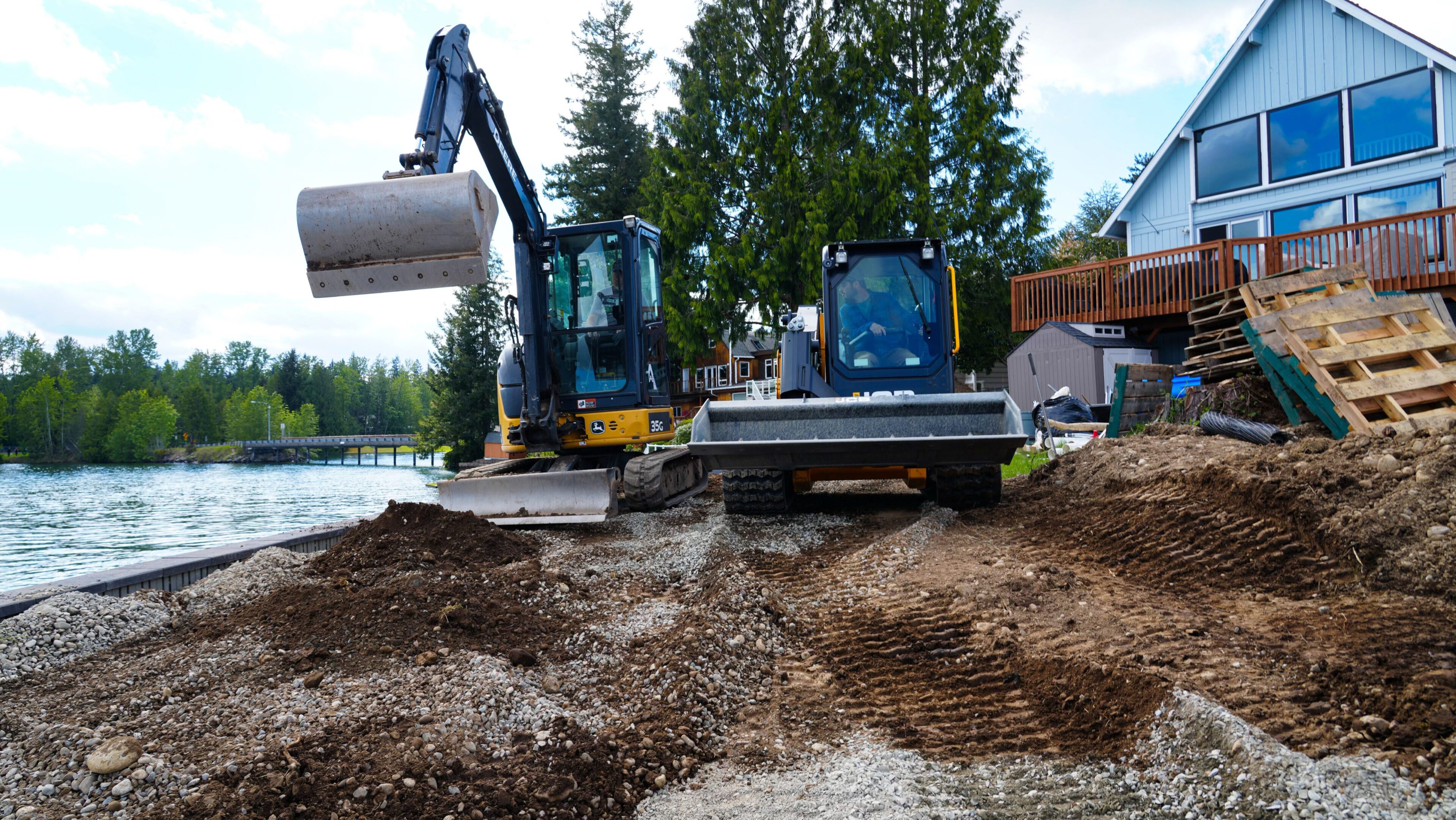 Excavators moving gravel at a construction site near trees.