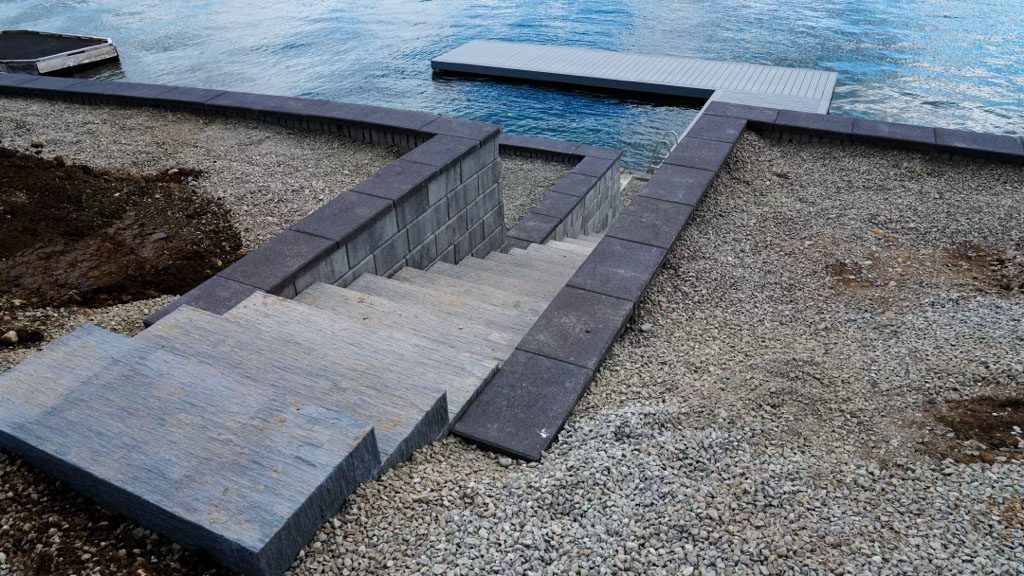 Modern outdoor steps and walkways beside a pool with gravel surroundings.