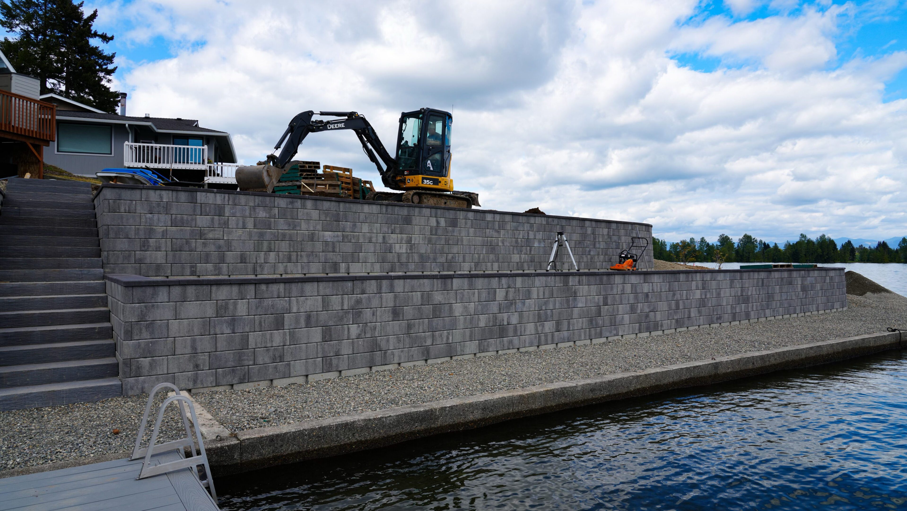 Excavator working on a stone retaining wall by the water.