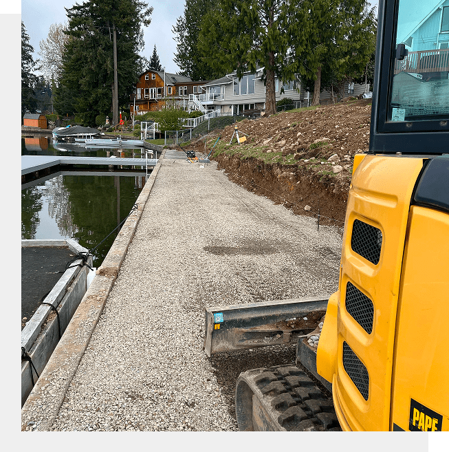 A construction vehicle working on a lakeside pavement near boats.
