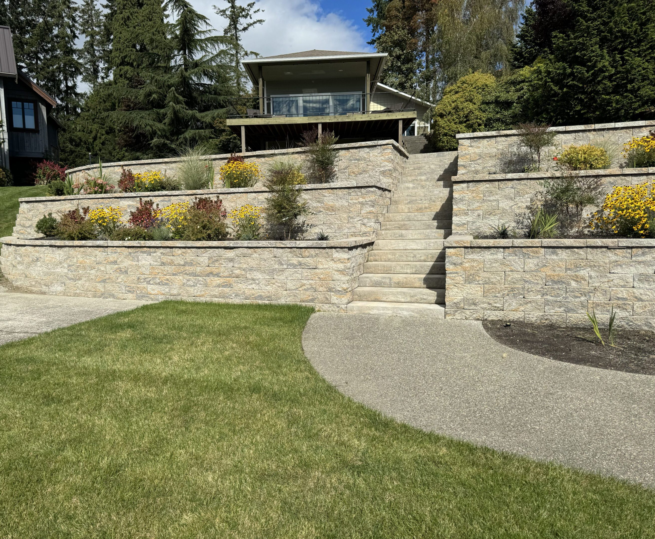 Stone retaining walls with steps lead to a garden gazebo surrounded by greenery.