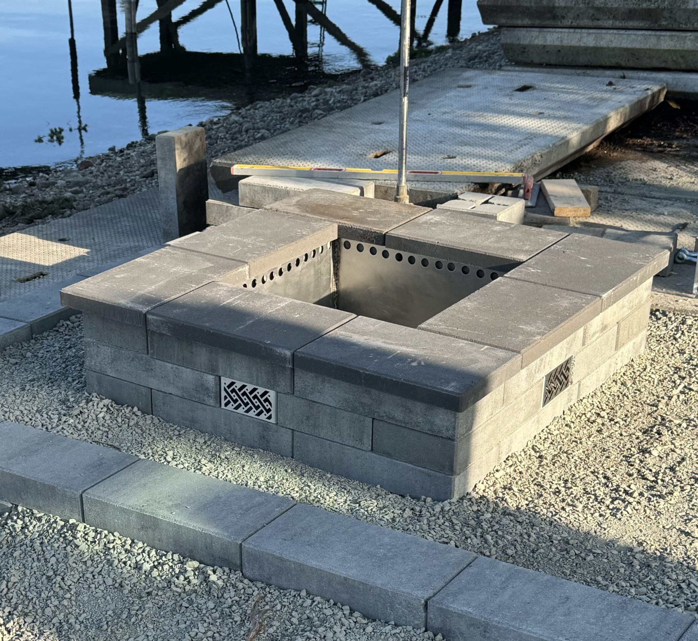 Stone outdoor grill near a wooden dock by the water.